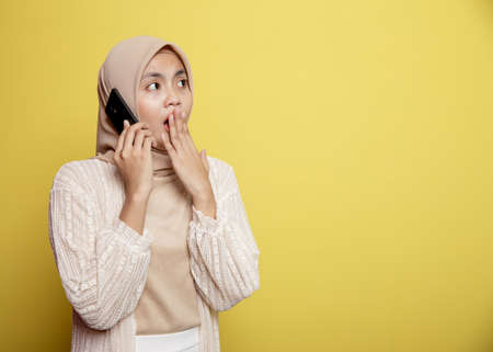 woman hijab with a calling phone shocked expression isolated on yellow backgroundの写真素材
