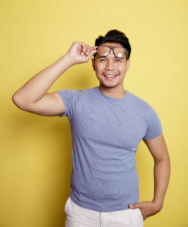 a happy man wearing a casual t-shirt with glasses isolated on a yellow color backgroundの写真素材