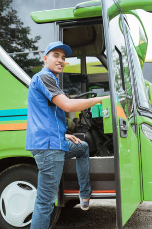 a bus driver in a uniform and a hat smiled at the camera as he stepped into the bus doorの写真素材