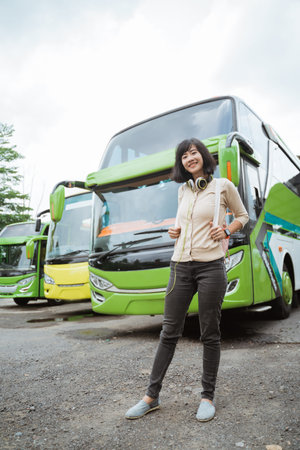 A young woman stands in a backpack and headphones smiling against the background of the bus