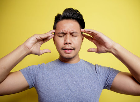 man wearing casual t-shirt dizzy expression holding head isolated on a yellow color backgroundの写真素材