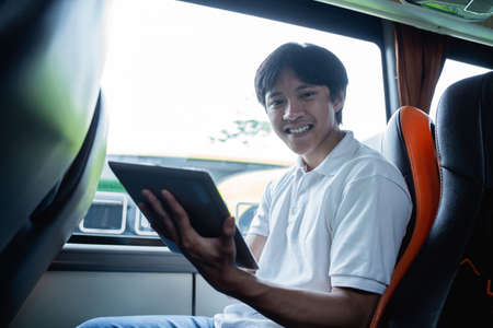 a man smiles while using a pad while sitting on a busの写真素材