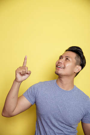 man wearing casual t-shirt smile expression showing blank space. thinking idea isolated on a yellow color backgroundの写真素材