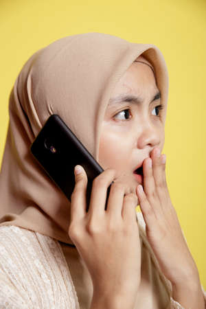 close up woman hijab with a calling phone shocked expression isolated on yellow backgroundの写真素材