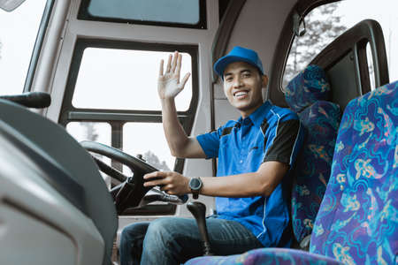 A male driver in uniform smiles at the camera as he sits down and waves at the busの写真素材