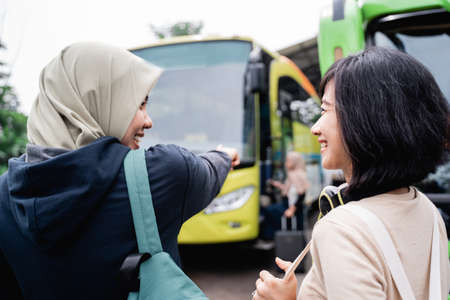 a woman in a headscarf with a finger pointing towards the bus while talking to a woman with headphones while going by busの写真素材