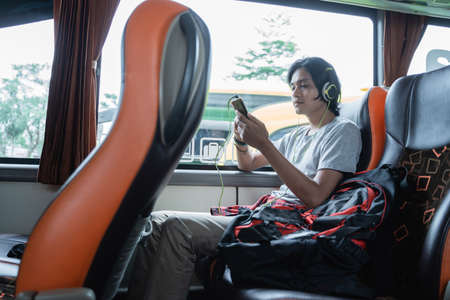 a man wearing headphones while listening music from a handphone while sitting by the window on a bus tripの写真素材