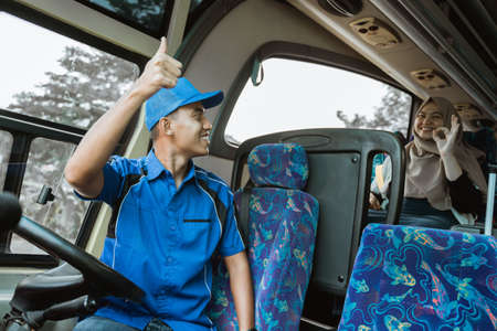A male driver in a blue uniform gave the passengers a thumbs-up as a signal for the bus to leave while sitting on the busの写真素材