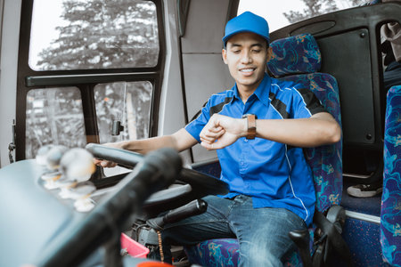 A male bus driver in blue uniform looks at his watch while sitting driving in the busの写真素材
