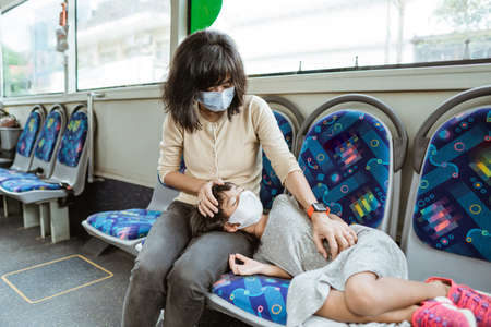 Asian mother wearing a mask along with a daughter who sleeps on a bench during a bus tripの写真素材