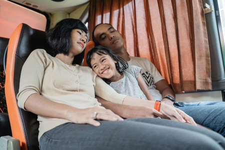 a little girl smiled while on the lap of her parents who slept while sitting on the bus seat during the tripの写真素材