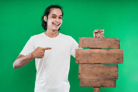 Asian man pointing and presenting something wooden board blank to the camera, isolated on green backgroundの写真素材