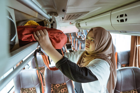 a woman in a headscarf puts her bag on a shelf while standing on the bus