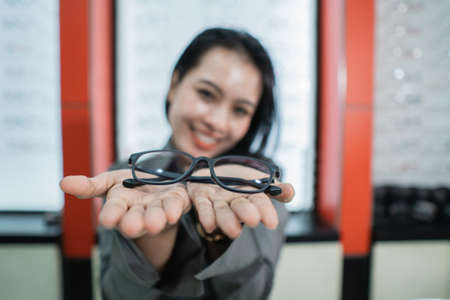 a beautiful woman is posing holding glasses against the background of a glasses display case in an eye clinicの写真素材