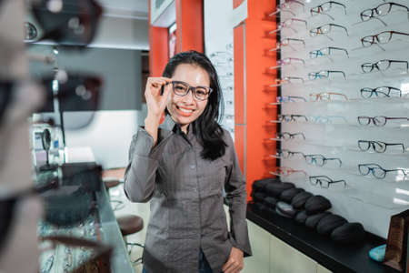 a beautiful woman posing wearing glasses against the background of an eyeglass display case in an eye clinicの写真素材