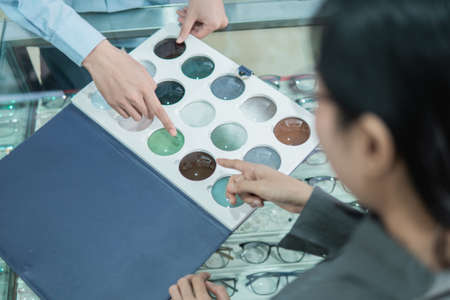 a female customer with a finger pointing to a lens sample when choosing a lens type at an opticianの写真素材