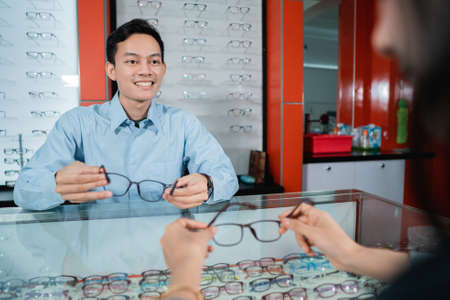 an eye clinic employee is serving female consumers when choosing glasses to use in an eye clinicの写真素材