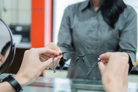 selective focus of the hands of a shop assistant giving a pair of glasses to the hands of a customer in an opticianの写真素材