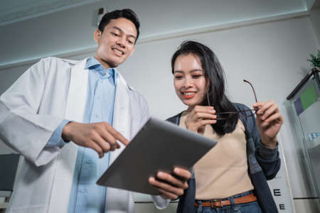 A male doctor is giving the results of an analysis to a female patient who has had an eye exam at an eye clinicの写真素材