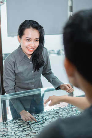 a shop assistant shows a pair of glasses in the window to a customer at an opticianの写真素材