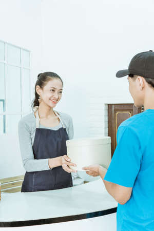 smiling young female shopkeeper receiving a package from courierの写真素材