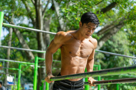 A muscular man who does pull ups to work his biceps and triceps muscles while exercising outdoors in...