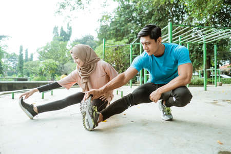 a man and a veiled girl in sportswear perform leg stretches before workout in the parkの写真素材