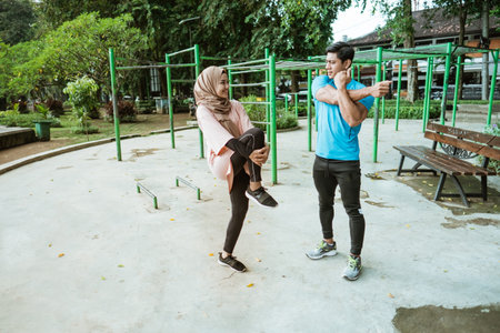 a young man and a girl in a veil chatting while standing doing warm-up movements before exercising...