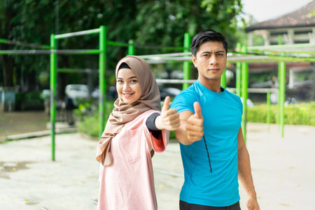 portrait of Muslim couples stand back to back exercising in the park showing thumb upの写真素材