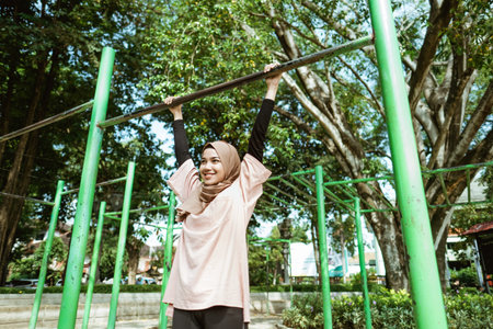 a girl in veil doing pull up to improve lung ability and lose weight by exercising outdoors in the...
