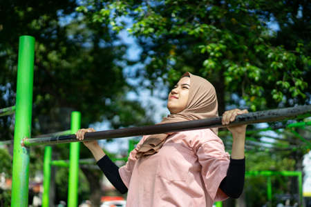 a girl in a veil does pull ups to work out her hand muscles in the parkの写真素材