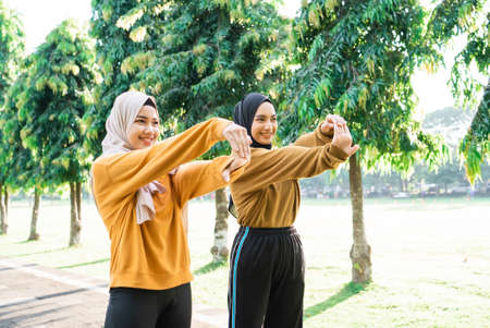 two veiled Muslim girls stretch their hands before jogging and outdoor sports in the parkの写真素材