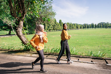 two Asian girls in headscarves enjoy jogging together while chatting in the afternoon in the garden...