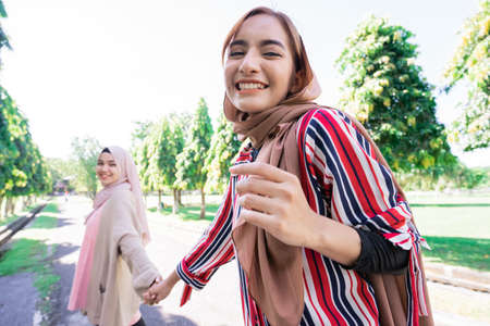 Two friends enjoying the summer sun and holding hand walking in the parkの写真素材
