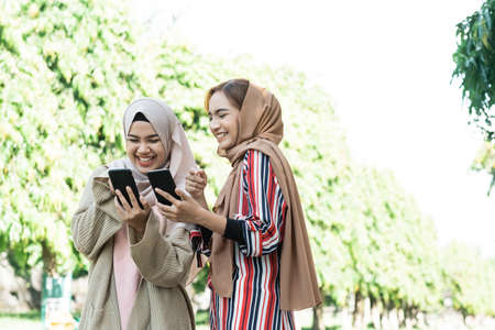 young asian muslim woman in head scarf meet friends and using phone in the parkの写真素材