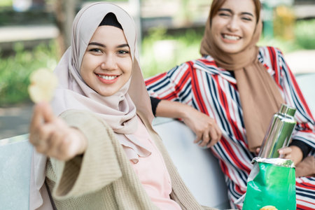 happy muslim young woman with friend enjoy their snack while relaxing in the parkの写真素材