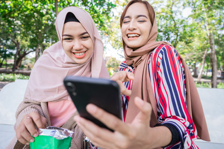 young asian muslim woman in head scarf meet friends and using phone in the park