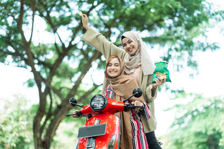 portrait of happy muslim friend riding motorcycle scooter together outdoorの写真素材