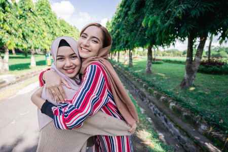Two muslim girls hug on the sidewalk. Feel joyfull and happy together.