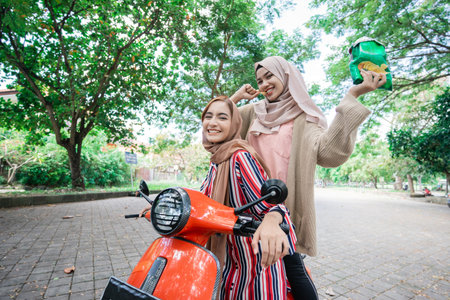 portrait of happy muslim friend riding motorcycle scooter together outdoor