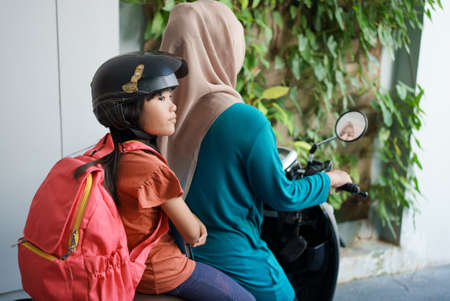 muslim mother taking her daughter to school by motorcycle in the morning. asian primary student back to schoolの写真素材