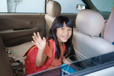 asian primary pupil student sitting in the car and waving good bye while going to school in the...