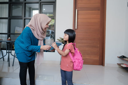 portrait of indonesian primary school female student shake and kiss her muslim mothers hand before...