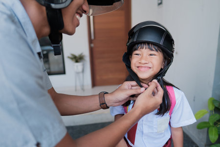 father taking his daughter to school by motorcycle in the morning. fasten the helmet. asian primary...