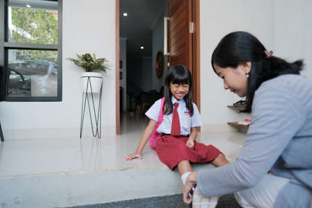mother help her daughter to wear a shoes in the morning while preparing to go to schoolの写真素材