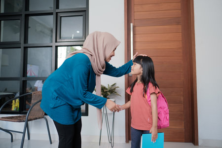portrait of indonesian primary school female student shake and kiss her muslim mothers hand before going to schoolの写真素材