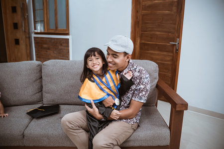 Kindergarten graduation. asian father embrace his daughter at home after graduation ceremony at homeの写真素材