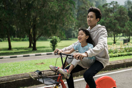 asian Older brother take his sister on fun bike riding in the parkの写真素材