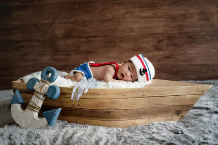 newborn baby boy wearing a white and blue sailor hat. He is sleeping on his back in a tiny boat.の写真素材