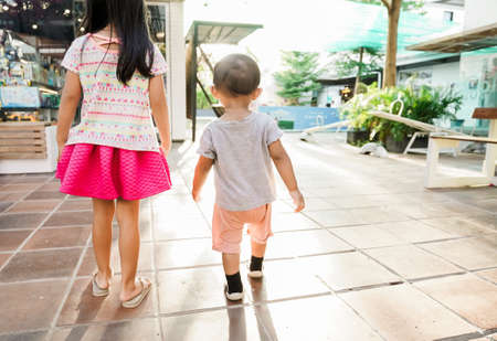 brother and sister kid walking together shot from behindの写真素材